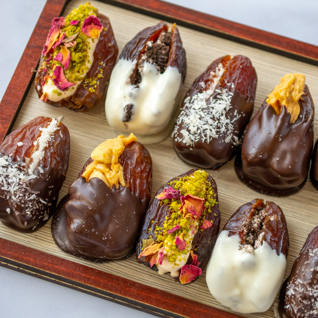 Four varieties of stuffed Medjool Dates: coconut dipped in chocolate, peanut butter with peanuts dipped in chocolate, pistachios with cream and edible flowers, and crushed Oreos dipped in white chocolate.