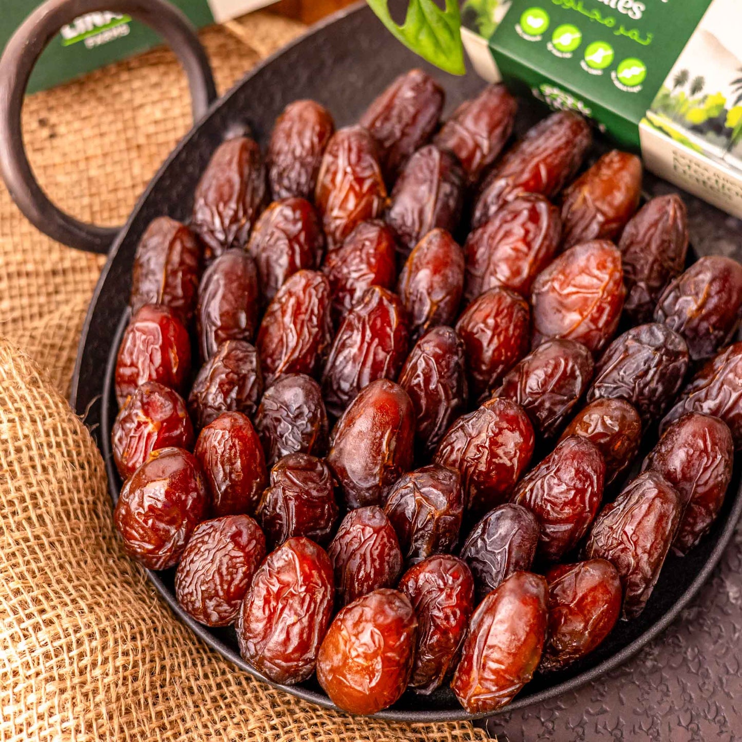 A plate full of extra juicy medjool dates with the Linah farms' extra juicy medjool dates box peeping from the corner of the photo