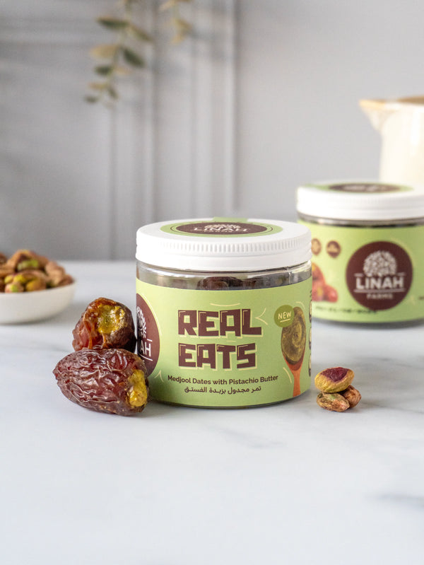 A jar of Pistachio Butter Stuffed Medjool Dates with two dates beside it, showcasing the smooth pistachio filling and chewy Medjool texture for a delicious, wholesome snack.